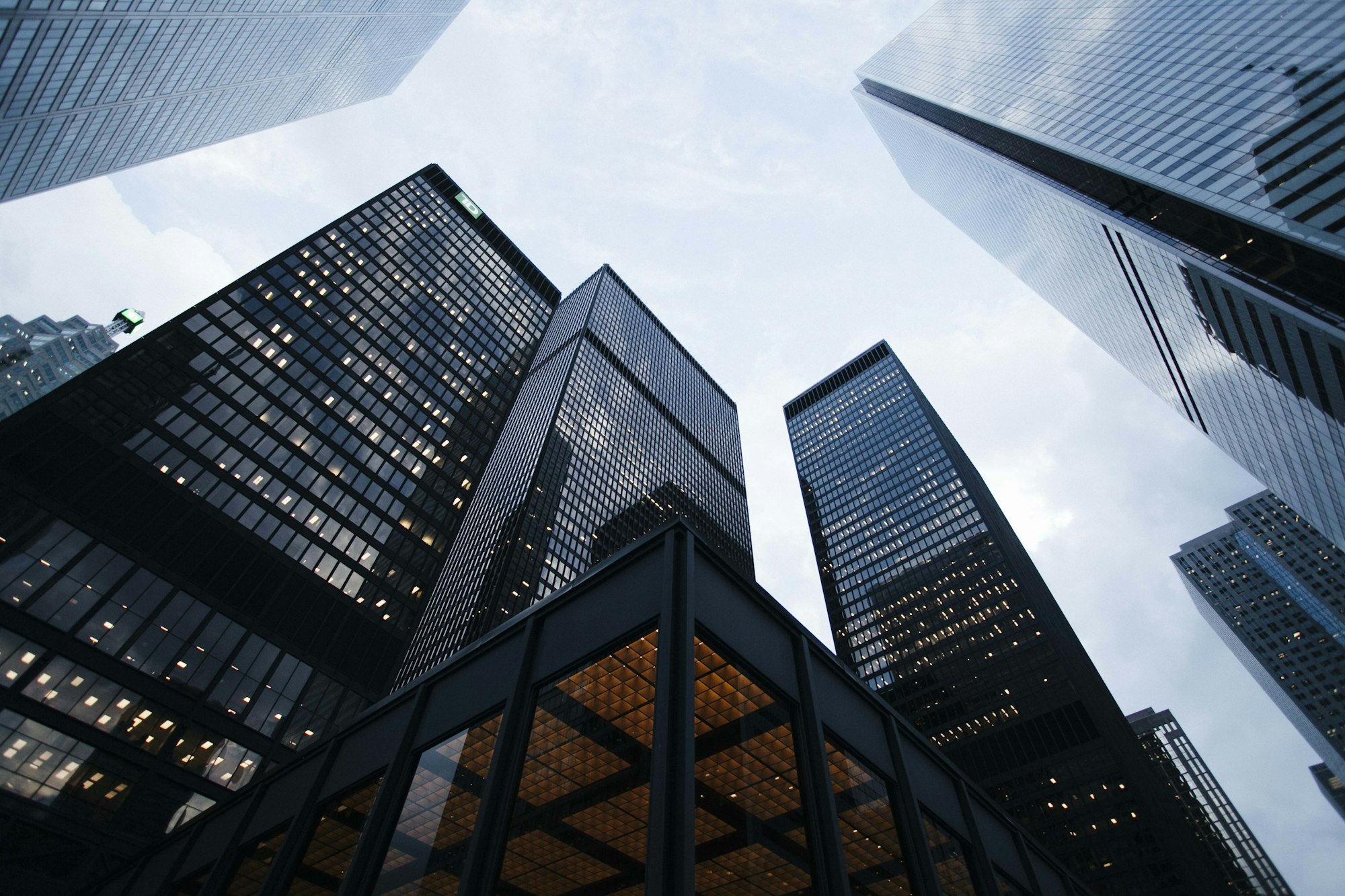 Generate an image of: A sleek, jet-black skyscraper exterior with yellow glowing windows at dusk, looking up from the ground, geometric perfection, hyper-detailed